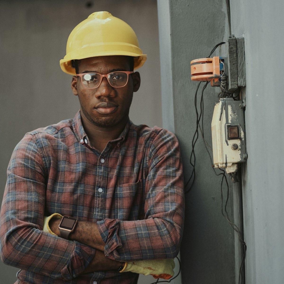 An engineer in a yellow hard hat and checked shirt stands with arms folded.