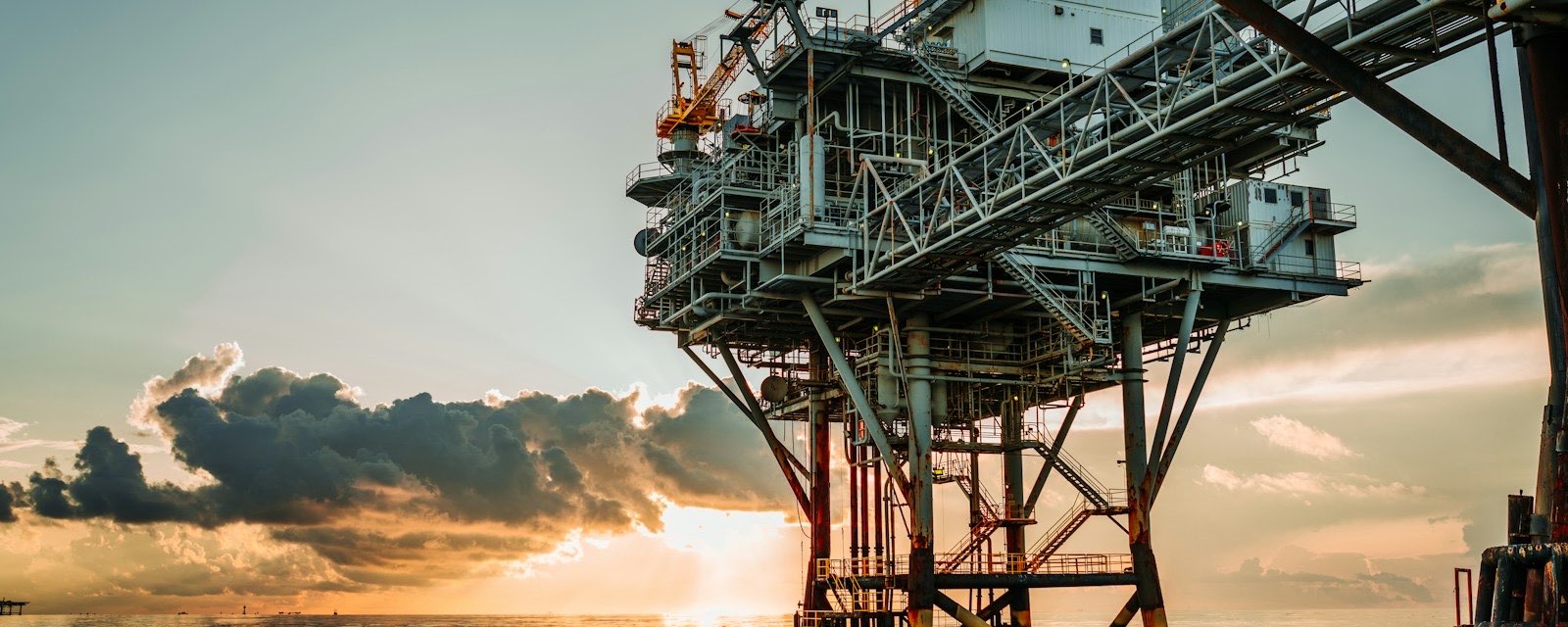 An offshore platform on steel legs above calm water at sunrise, with clouds lit gold on the horizon.