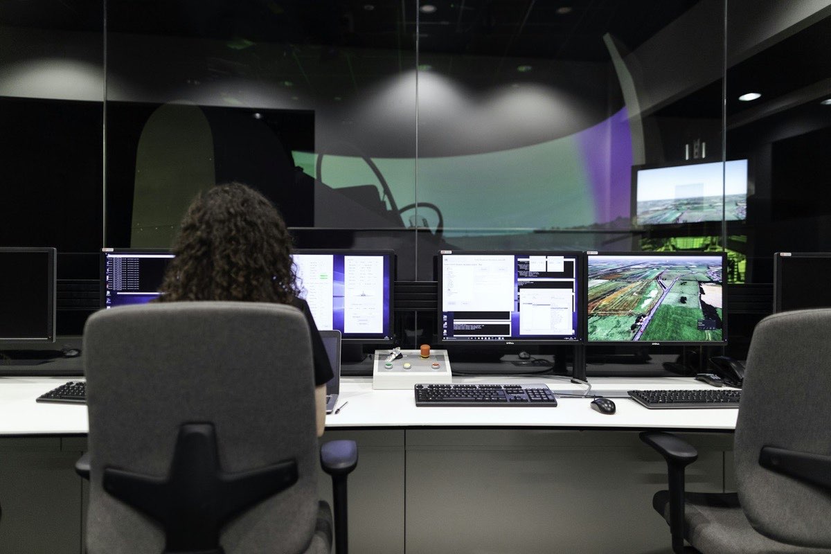 An engineer seated at a bank of monitors in a modern operations room, with a large curved display ahead.