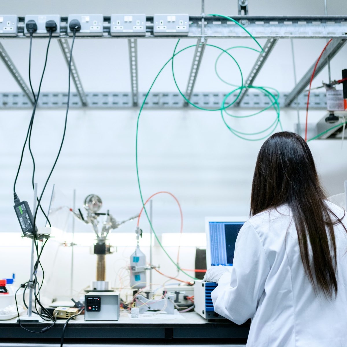 A scientist in a lab coat at a laboratory bench with glassware and a laptop.